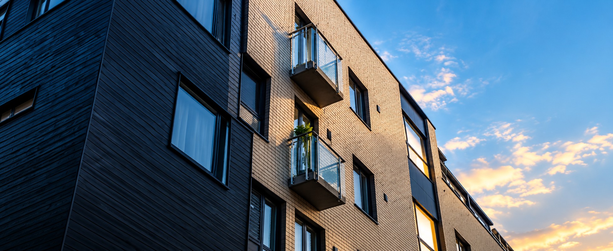 Flerbostadshus i kvällssol mot blå himmel